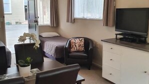 A compact room with a bed, a television, a desk with a chair, and a small table with a potted plant.
