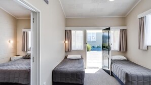 A room with two beds, a door leading outside, and a window with curtains.