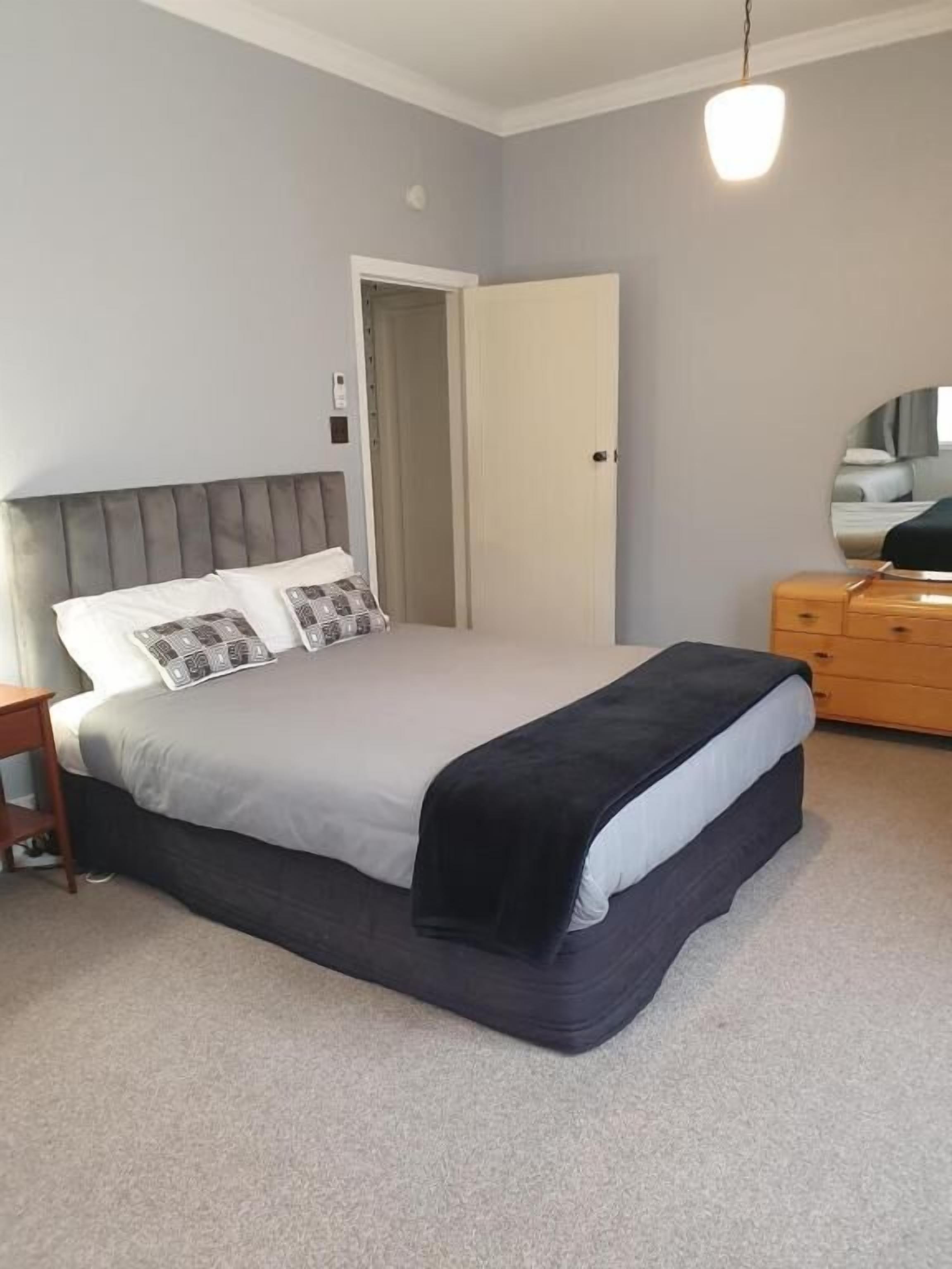 Un dormitorio con cama, cómoda, espejo y puerta.