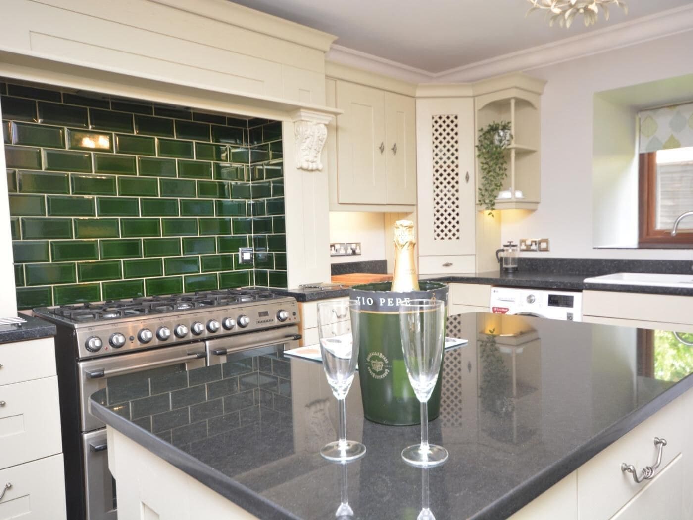 A kitchen with a gas stove, a green-tiled backsplash, and two champagne glasses on the counter.