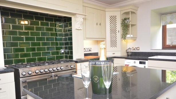 Et køkken med en gasblus, et backsplash med grønne fliser og to champagneglas på bordet.