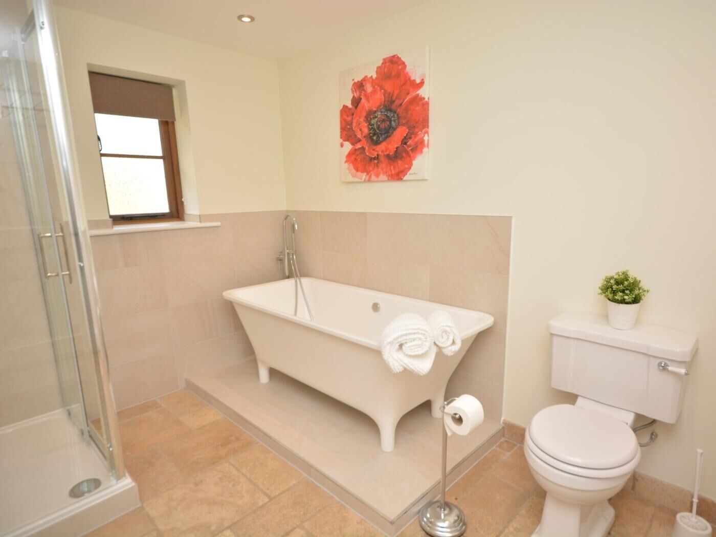 Ein Badezimmer mit einer freistehenden Badewanne, einer Toilette, einer Duschkabine und einem Blumentopf.