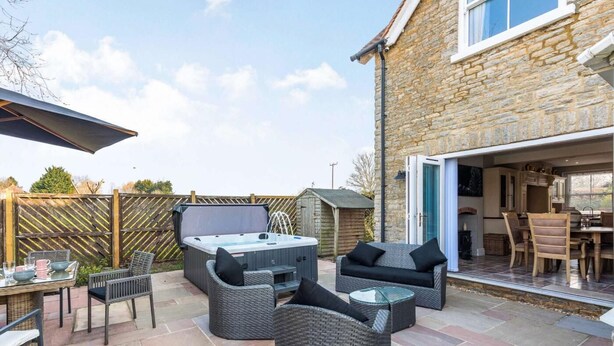 A patio with outdoor furniture, a hot tub, and a stone building with a glass door. - 5 Bed in Bicester (oc-87367) (Chesterton)