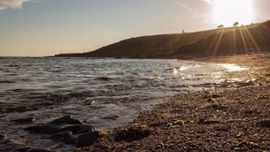 Ein Strand mit Wellen, einer felsigen Küste und einer entfernten Hügelkette mit einer Struktur.