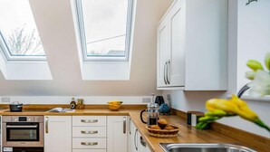 Eine moderne Küche mit Oberlichtern, einem Bosch-Ofen, weißen Schränken und einer Holz Arbeitsplatte.