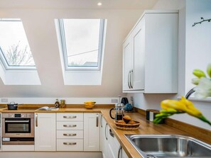A modern kitchen with skylights, a Bosch oven, white cabinetry, and a wooden countertop. - 1 Bed in Plymouth (oc-85355) (Wembury)