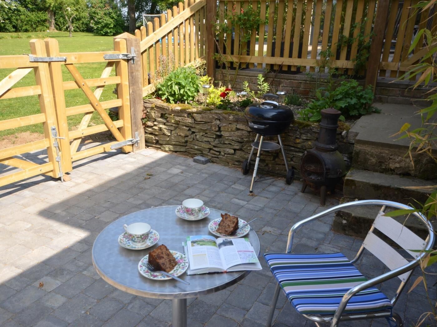 Eine Terrasse mit Tisch, der für Tee gedeckt ist, einem Grill und einer Steinmauer.