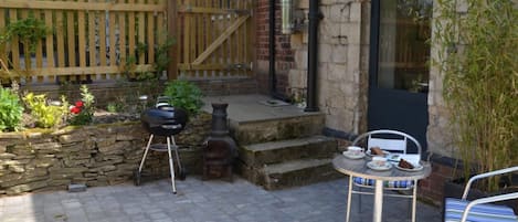 Une terrasse avec un barbecue, une table et des chaises, et un mur en pierre.