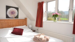 A bedroom with a bed, a nightstand, a window with curtains, a radiator, and a painting on the wall. - 1 Bed in Gloucester (oc-oldbn) (Upton Saint Leonards)