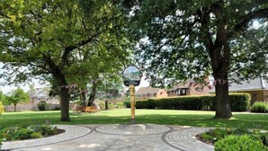 A circular stone pathway leading to a central signpost in a park-like setting with trees and a lawn. - 1 Bed in Gloucester (oc-oldbn) (Upton Saint Leonards)