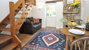 A staircase, a black leather sofa, a dining table with plates, a fruit bowl, and a stone wall. - 1 Bed in Gloucester (oc-oldbn) (Upton Saint Leonards)