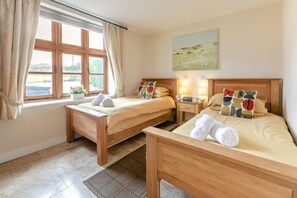 A room with two wooden beds, a window with curtains, a painting on the wall, and a small bedside table with a lamp. - 2 Bed in Bideford (oc-swabr) (Higher Clovelly)