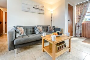 Ein Wohnzimmer mit grauem Sofa, einem Holztisch mit Obstschale und einem Gemälde an der Wand.