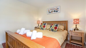 A neatly made bed with towels, a wooden headboard, a bedside table with a lamp, and a wall art piece. - 2 Bed in Bideford (oc-swabr) (Higher Clovelly)