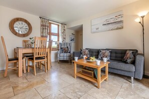 A living room with a sofa, a dining table with chairs, a wooden coffee table, and a wall clock. - 2 Bed in Bideford (oc-swabr) (Higher Clovelly)