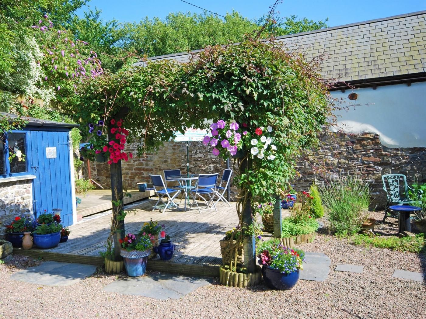 A garden area with a wooden deck, outdoor seating, and a blue shed.