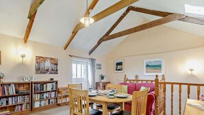 A cozy room with a wooden dining table, chairs, a bookshelf, and a red sofa. - 4 Bed in Penzance (oc-holba) (Saint Buryan)