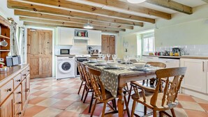 A kitchen with a dining area, wooden beams, a washing machine, and a tiled floor. - 4 Bed in Penzance (oc-holba) (Saint Buryan)