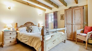 A bedroom with a four-poster bed, wooden beams on the ceiling, a nightstand with a lamp, a wicker chair, and a wardrobe. - 4 Bed in Penzance (oc-holba) (Saint Buryan)
