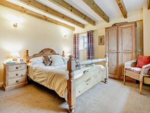 Ein Schlafzimmer mit Himmelbett, Holzbalken an der Decke, einem Nachttisch mit Lampe, einem Korbstuhl und einem Kleiderschrank.
