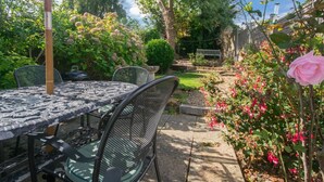 Eine Terrasse mit Tisch und Stühlen, umgeben von üppigem Grün und blühenden Pflanzen.