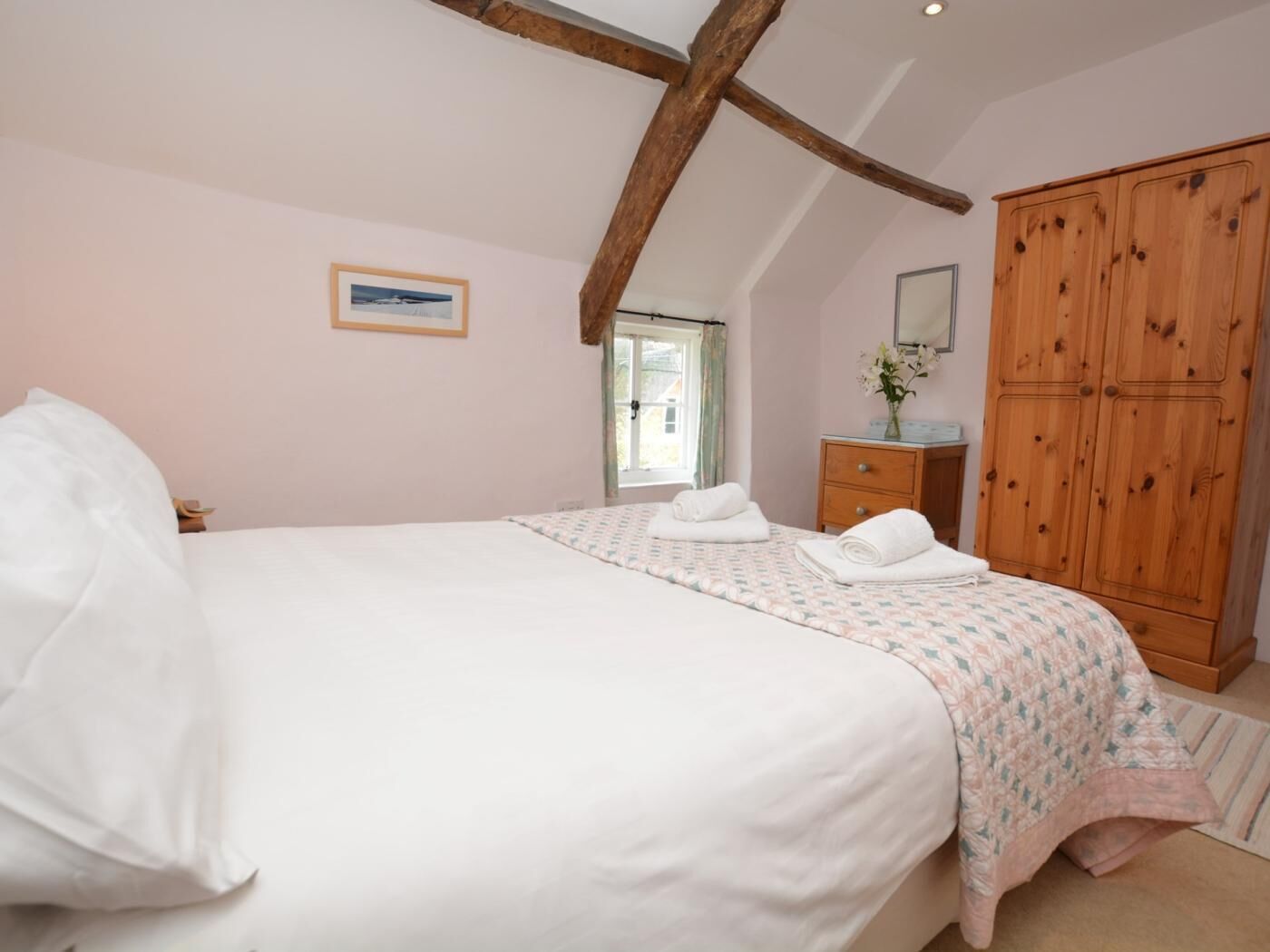A bedroom with a large bed, a wooden wardrobe, a small bedside table, and a window.