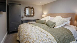 Un dormitorio con tragaluz, cama con ropa de cama floral, mesita de noche con lámpara y armario.