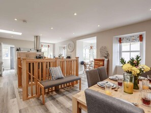 A spacious dining area with a wooden bench and table, a kitchen in the background, and a large window with a view. - 3 Bed in Burnmouth (oc-78485) (Burnmouth)