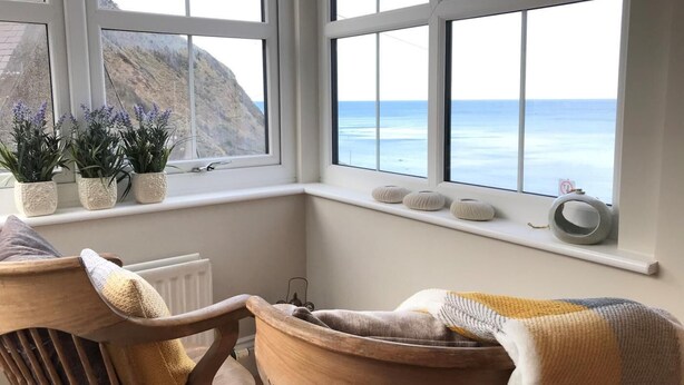 Una habitación con vistas al mar, un alféizar con plantas y un sillón con una manta.