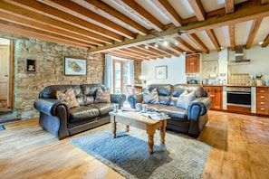 A spacious living area with leather sofas, a coffee table, and a stone wall. - 2 Bed in Penrith (oc-79466) (Kirkland)