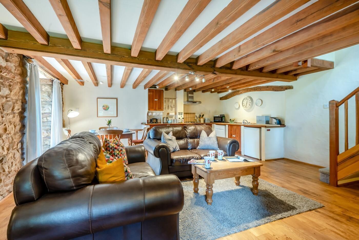 A cozy living room with leather sofas, a wooden coffee table, and a kitchen in the background.