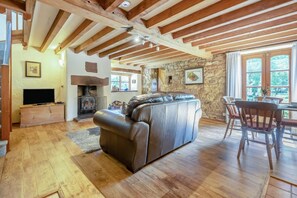 Ein geräumiges Wohnzimmer mit Kamin aus Stein, Holzbalken, einer Ledersofa und einem Essbereich mit Tisch und Stühlen.
