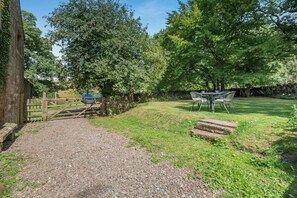 A gravel path leading to a wooden gate, a stone bench, a picnic table with chairs, and a grassy area with trees. - 2 Bed in Penrith (oc-79466) (Kirkland)
