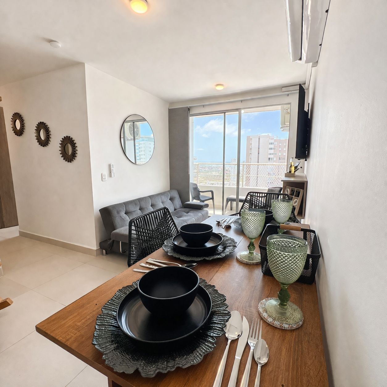 Een eethoek met een houten tafel voor vier personen, een grijze bank en een balkon met uitzicht.
