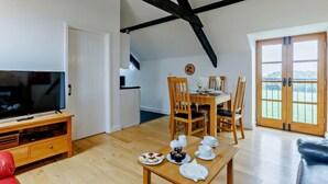A dining area with a table set for four, a television, and a red couch. - 2 Bed in Bideford (oc-housm) (Higher Clovelly)