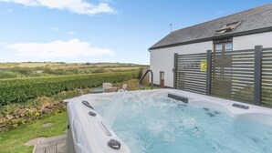 A hot tub with a wooden deck, a white building with a grey roof, and a countryside view. - 2 Bed in Bideford (oc-housm) (Higher Clovelly)