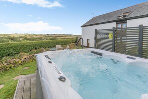 Ein Whirlpool mit Holzterrasse, ein weißes Gebäude mit grauem Dach und Blick ins Grüne.