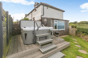 Ein Whirlpool und ein Grillplatz in einem Garten mit einer Holzdielen-Terrasse und einer Steinmauer.