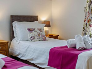 Quarto de hotel com cama, mesa de cabeceira, abajur e cortina florida.