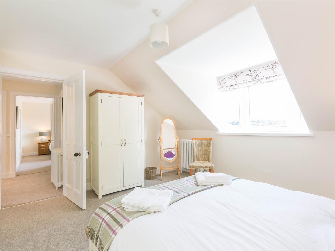 A bedroom with a bed, a wardrobe, a chair, a window, and a door leading to another room.