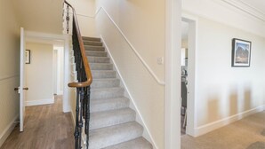 Una escalera con barandilla de madera, escalones alfombrados y una pared blanca.