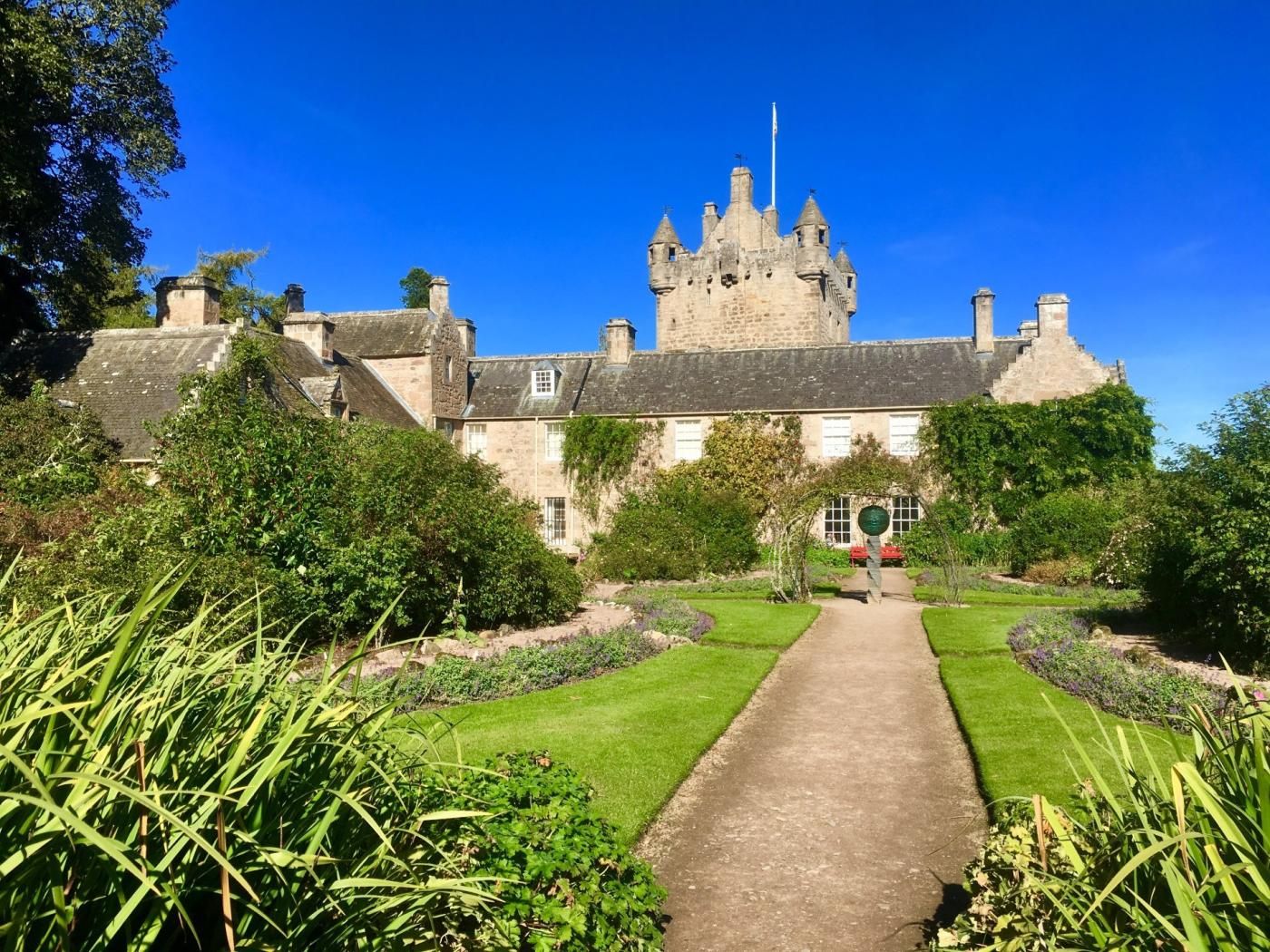 Een kasteel met een centraal torentje, omringd door verzorgde tuinen en een heldere lucht.