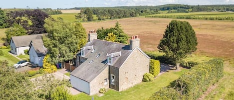 A large stone house with a sloped roof, surrounded by well-maintained lawns and trees.