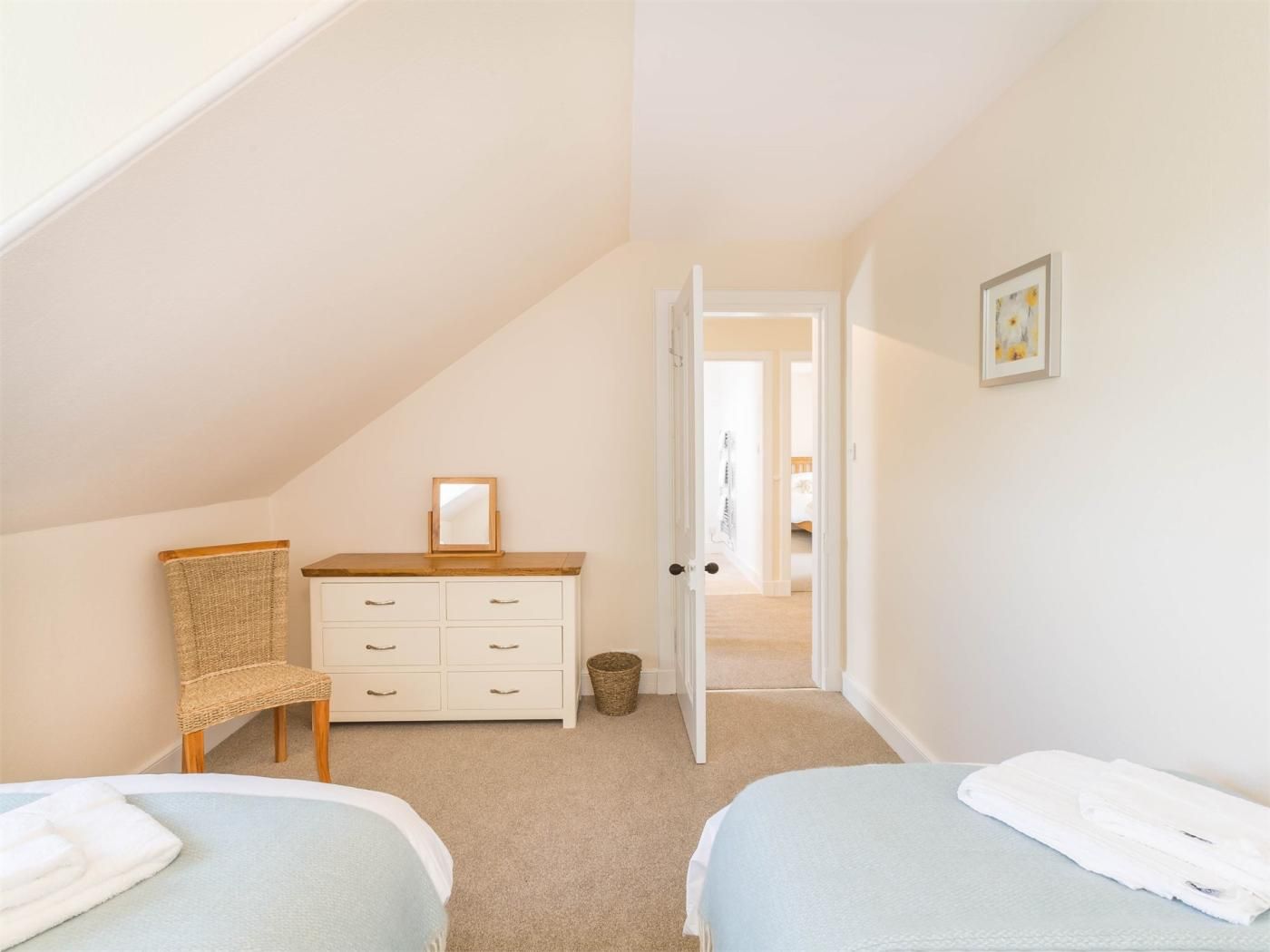 A bedroom with two beds, a dresser, a chair, and a door leading to another room.