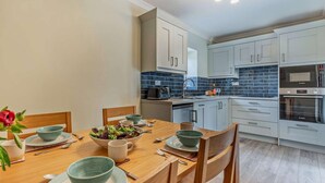 Uma cozinha moderna com armários brancos, um backsplash revestido de azulejos azuis e uma área de jantar com mobiliário de madeira.