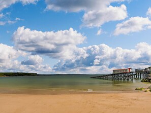 A beach with a pier extending into calm waters, a clear sky, and a distant shoreline. - 2 Bed in Tenby (oc-fb116) (Tenby)