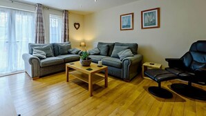 A living room with two grey sofas, a wooden coffee table, a black leather chair, and a small side table. - 2 Bed in Tenby (oc-fb116) (Tenby)