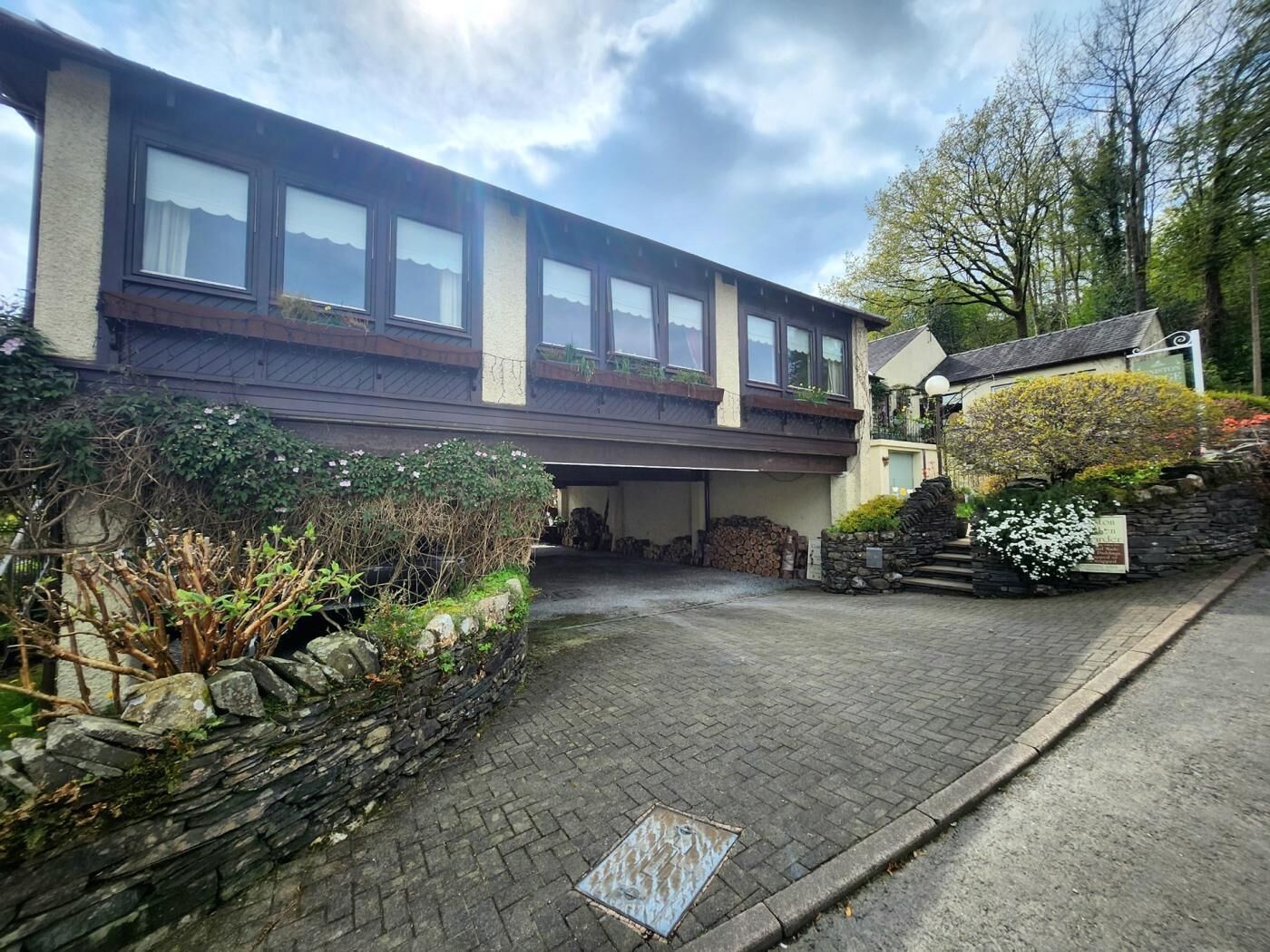 A two-story building with a stone facade, a garage, and a small garden area with plants and flowers.