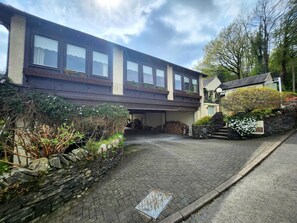 Ein zweistöckiges Gebäude mit einer Fassade aus Stein, einer Garage und einem kleinen Garten mit Pflanzen und Blumen.