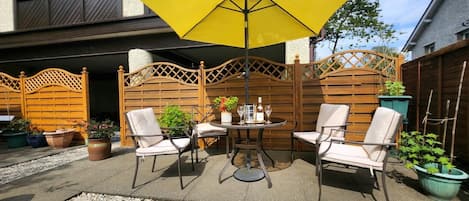 A patio with a table and chairs, a yellow umbrella, and potted plants.